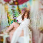 Woman sitting in sheer fabric during boudoir shoot surrounded by flowers