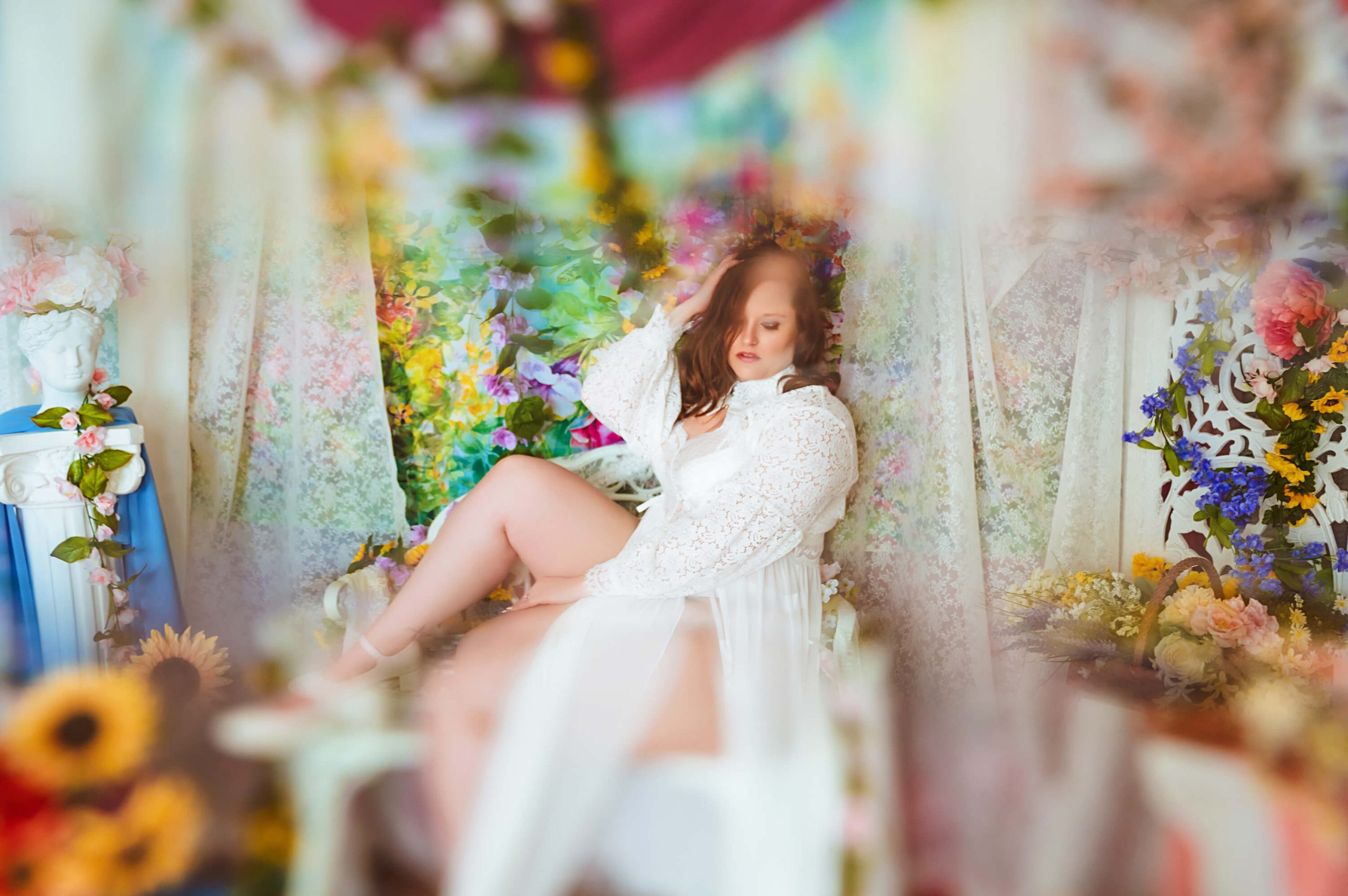Woman sitting in sheer fabric during boudoir shoot surrounded by flowers